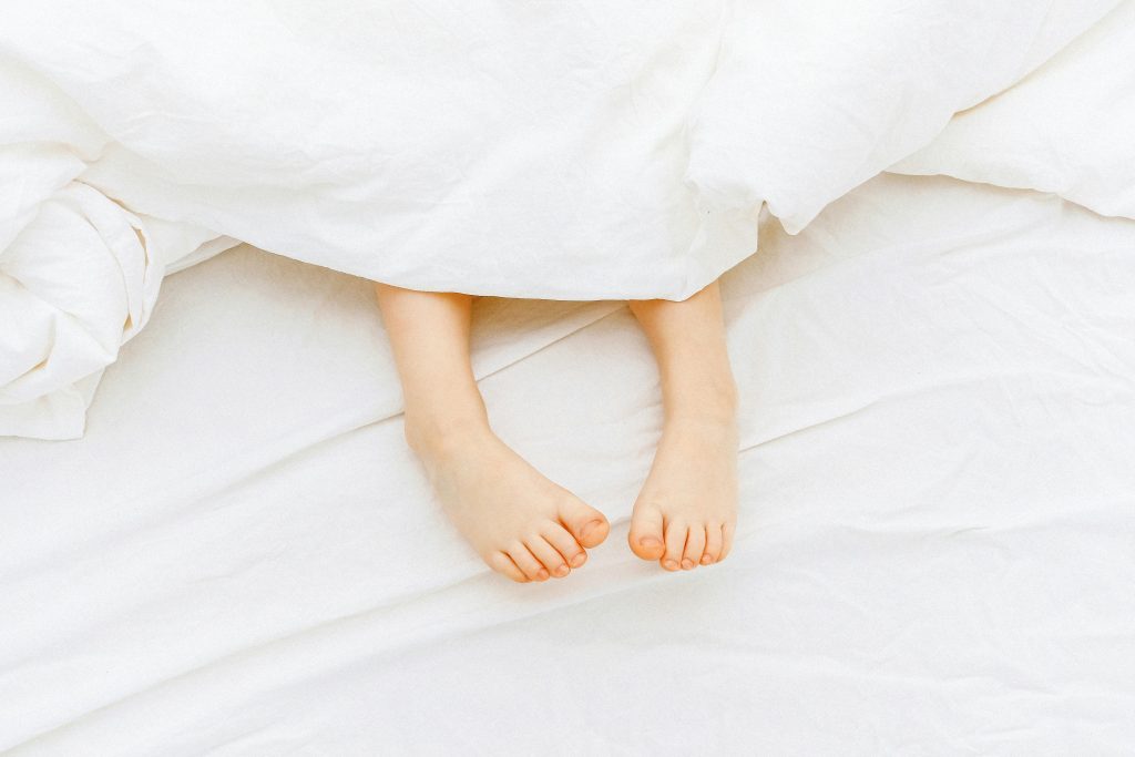 Cute child's feet sticking out from a white blanket, conveying warmth and comfort.